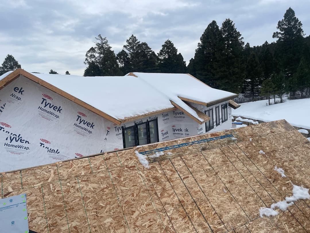 New home under construction with snowy roof and Tyvek house wrap in winter landscape.