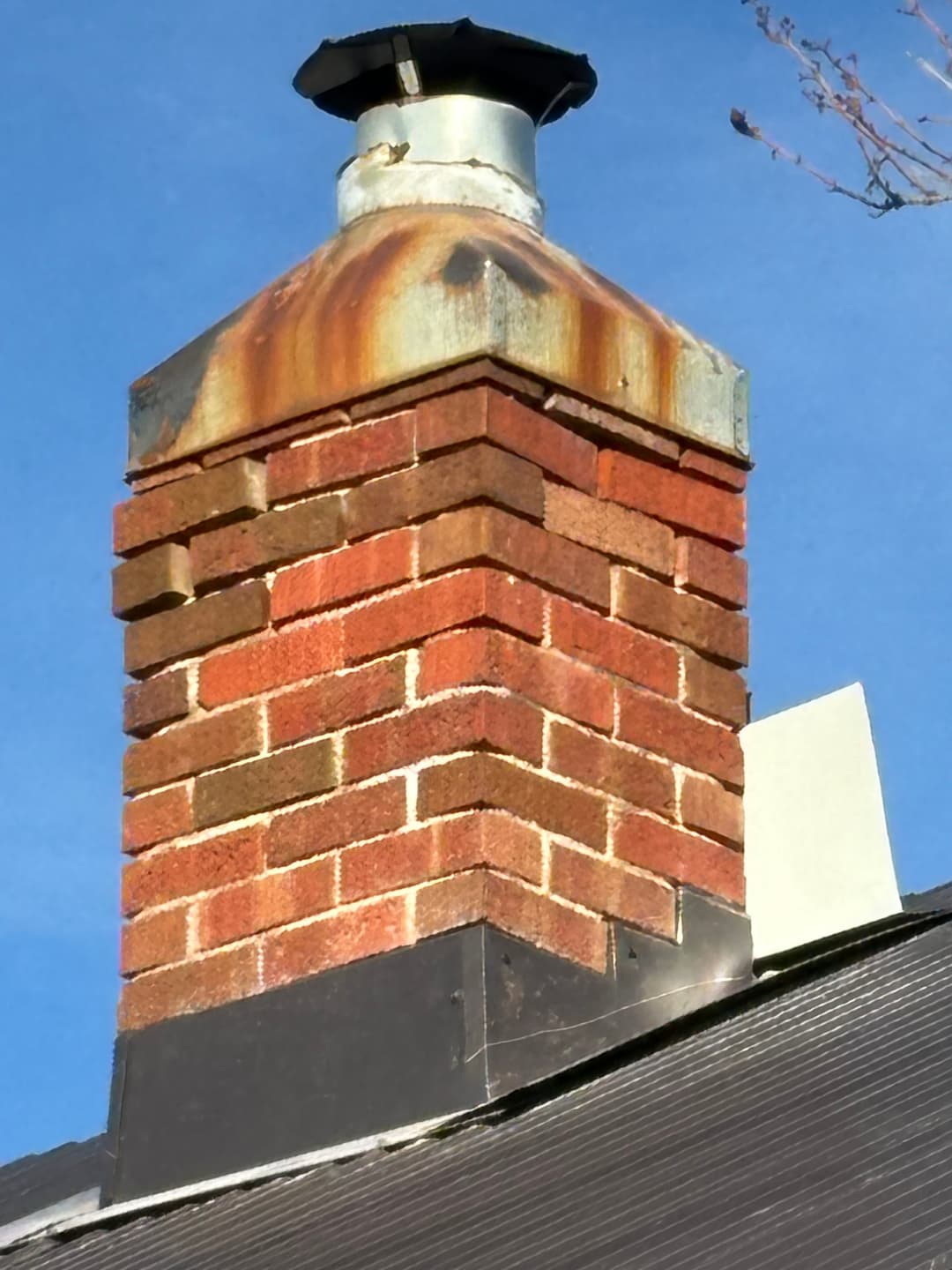 Chimney with rusted metal cap atop a brick structure against a blue sky.