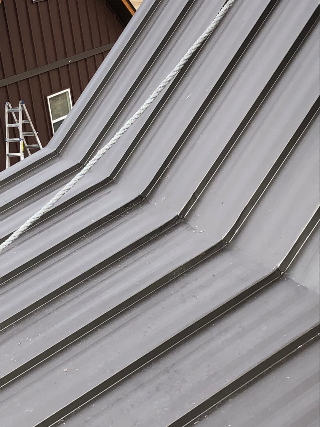 Metal roof with ribbed texture and rope, showcasing construction elements and a ladder nearby.