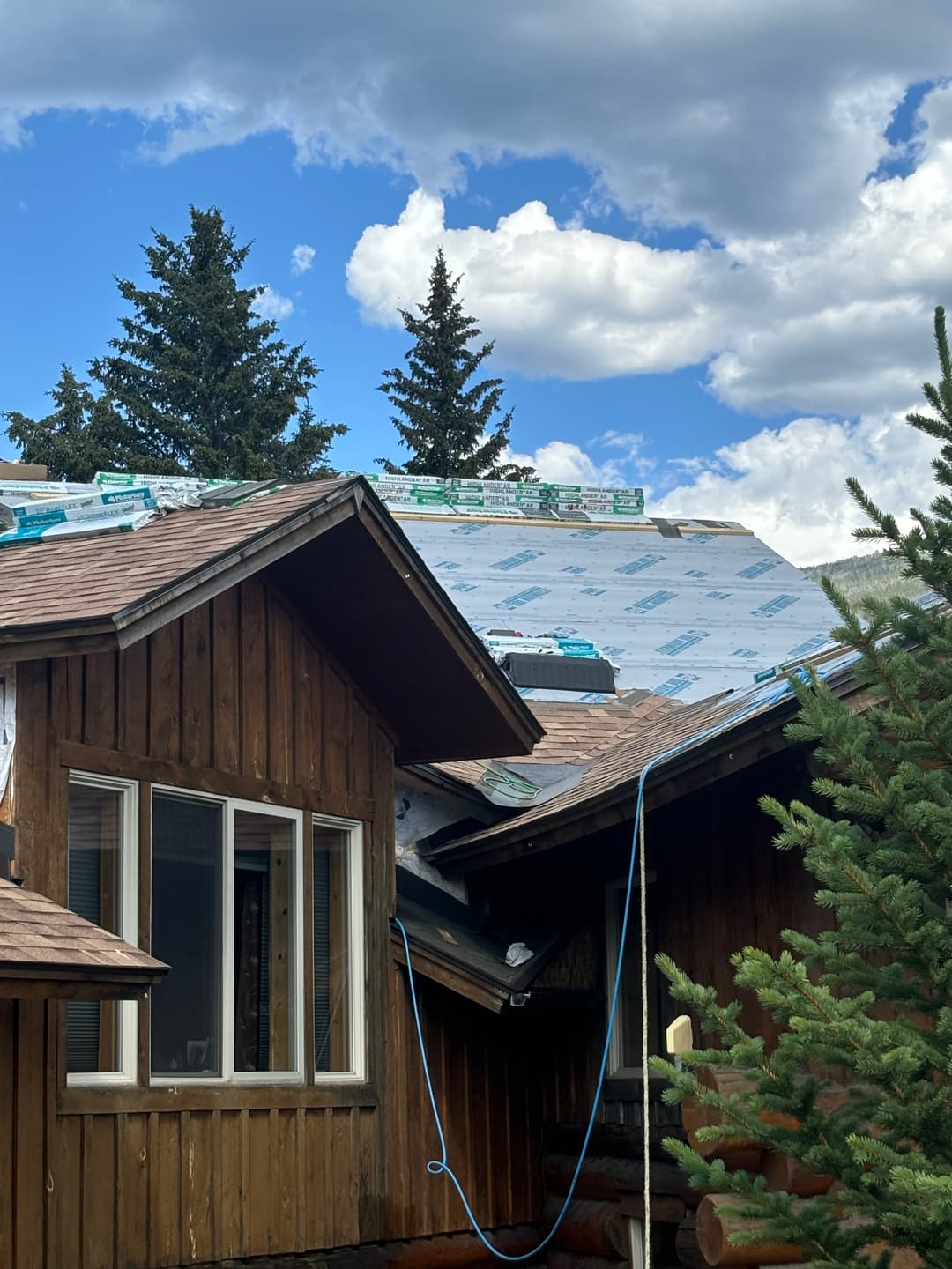 Roofing installation with materials on a house under a blue sky and scattered clouds.