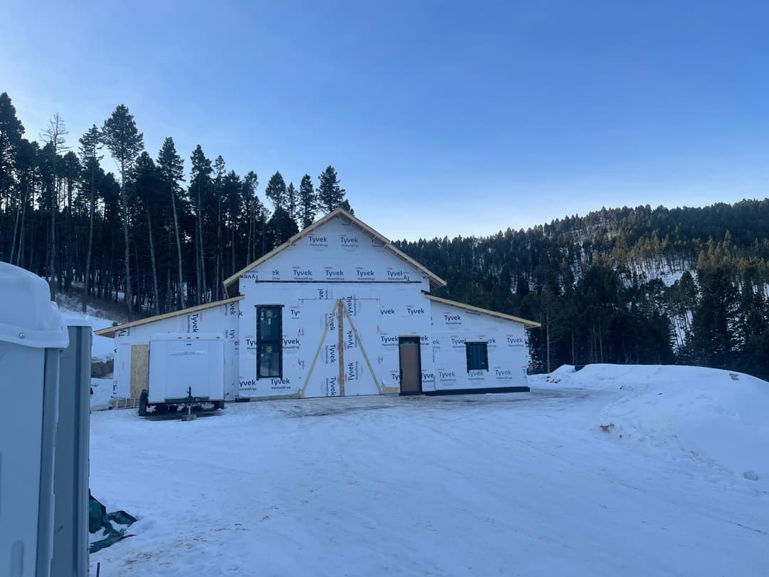 Newly constructed house wrapped in Tyvek in snowy mountain landscape with pine trees.