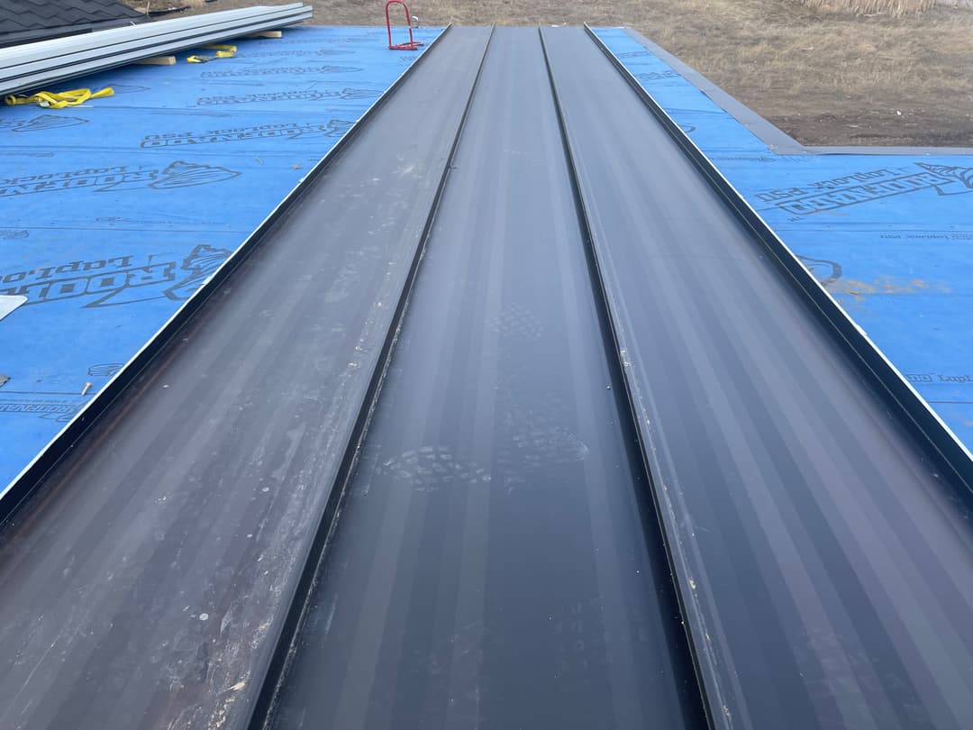 Metal roofing panels installed on a construction site with blue underlayment visible.