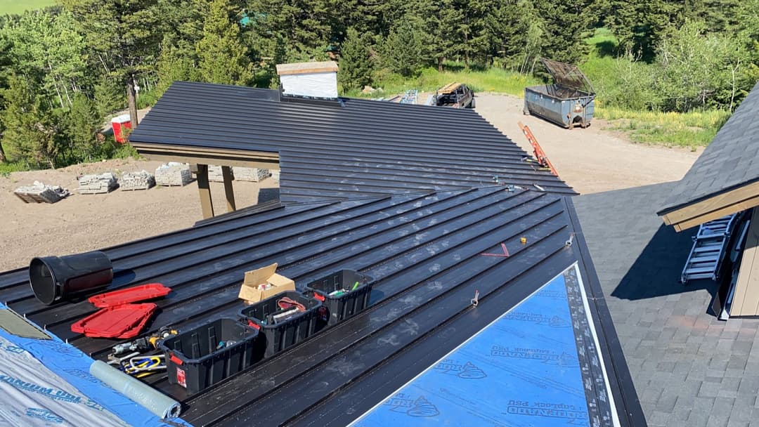 Residential metal roofing installation in a construction site with tools and landscape background.