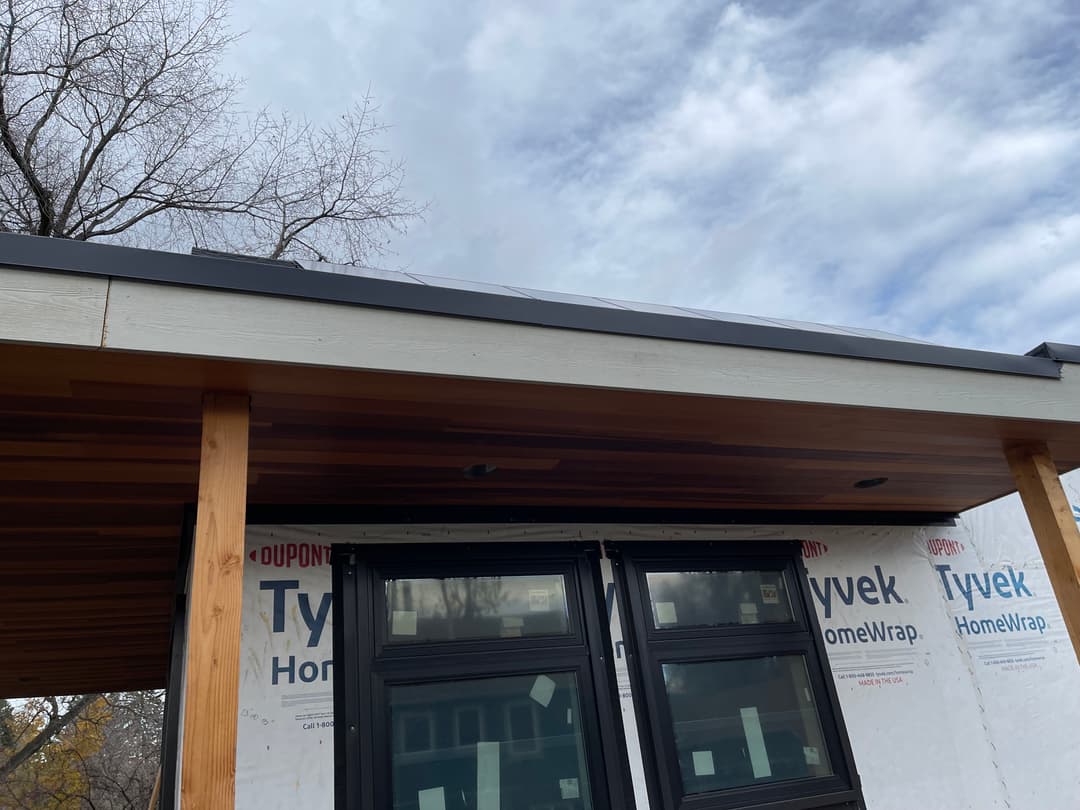 Modern home exterior with Tyvek HomeWrap and wooden overhang under a cloudy sky.