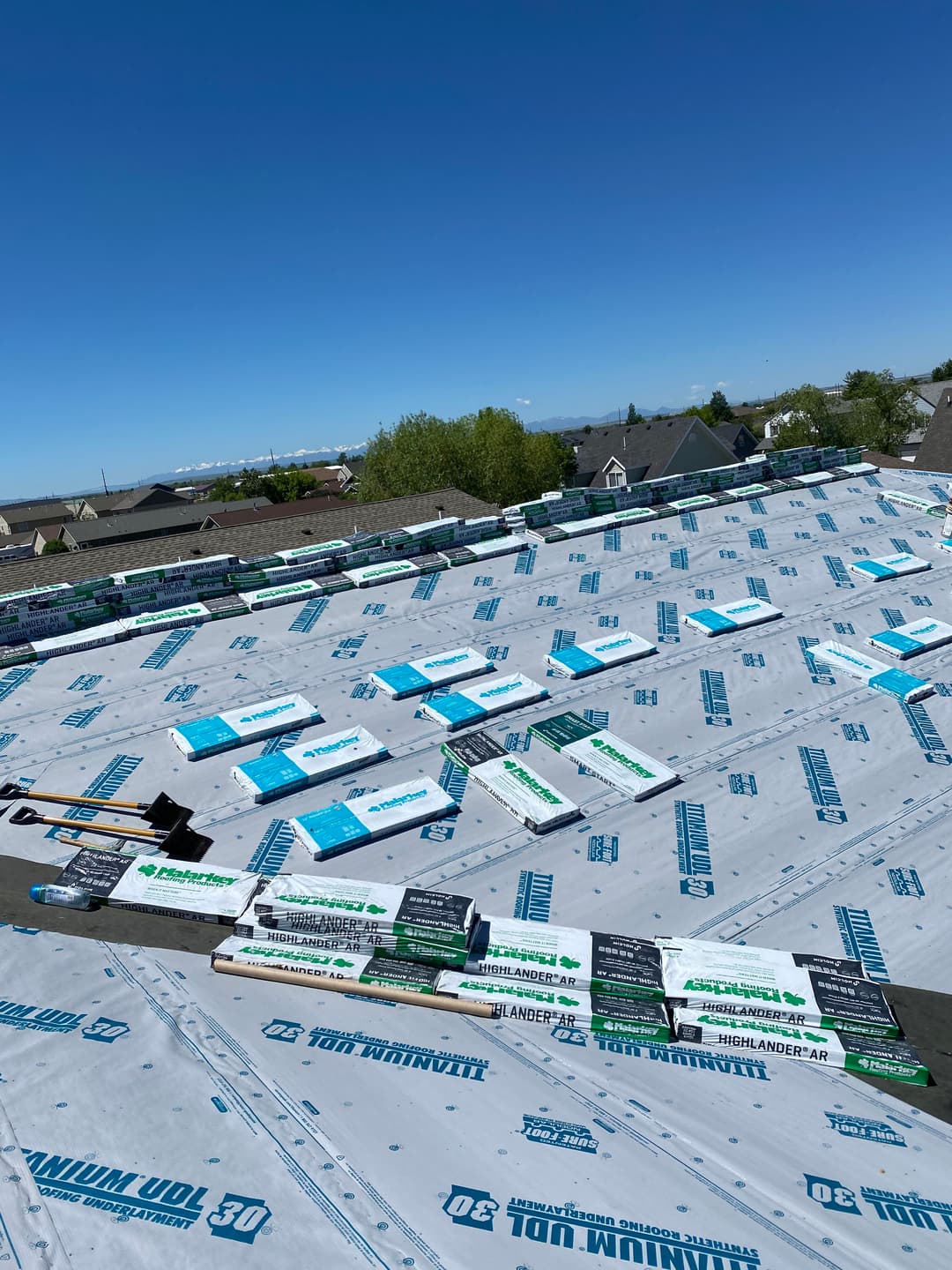 Roof underlay installation with roofing materials laid out on a residential building.