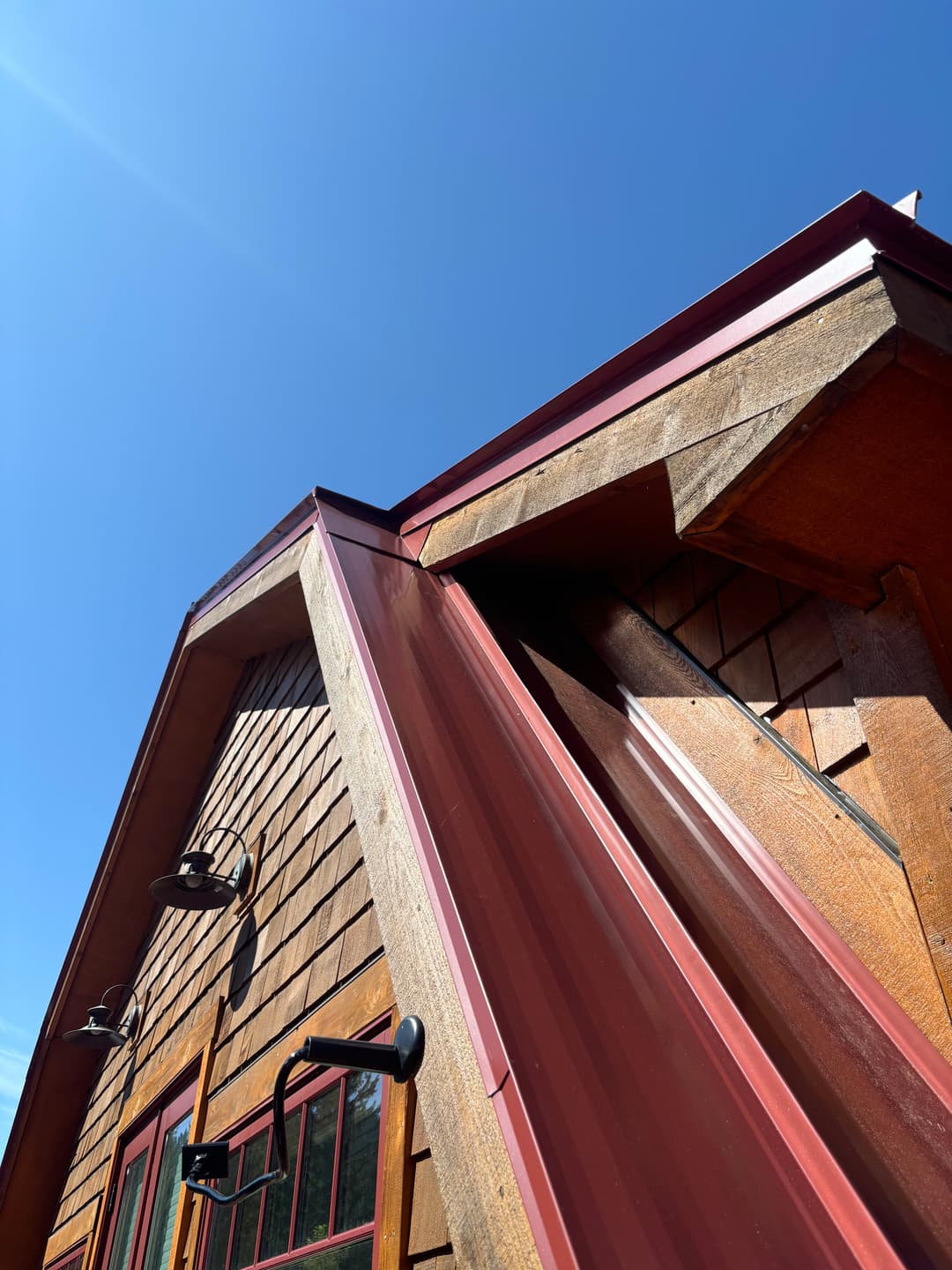 Modern wooden cabin exterior with a red metal roof against a clear blue sky.