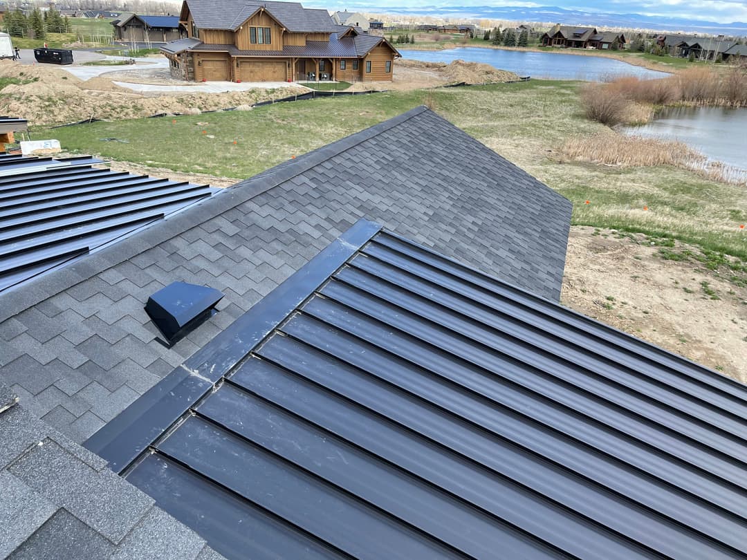 Aerial view of modern rooftops with shingles and metal panels near a lake and houses.