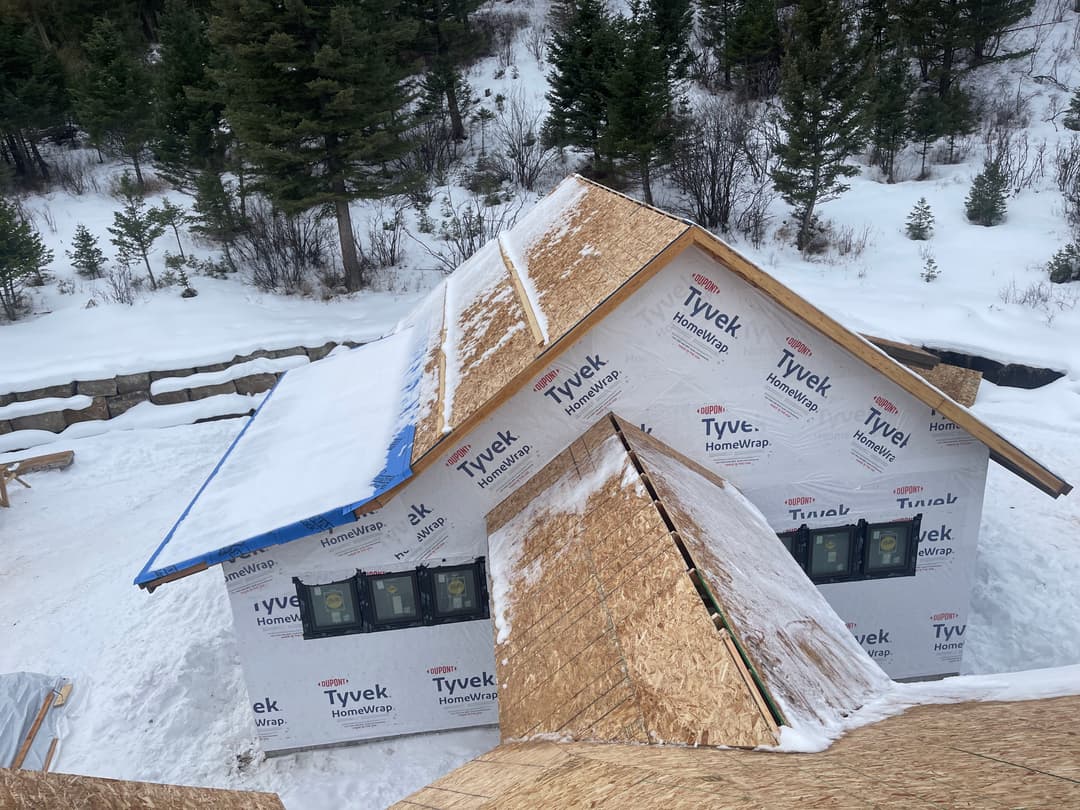 New roof installation on a house under construction in a snowy landscape surrounded by trees.