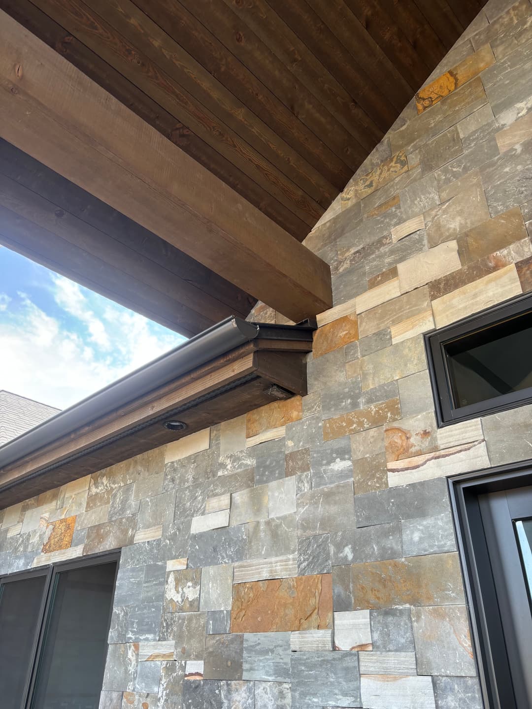 Modern architectural detail featuring stone wall and wooden overhang with seamless roofing.