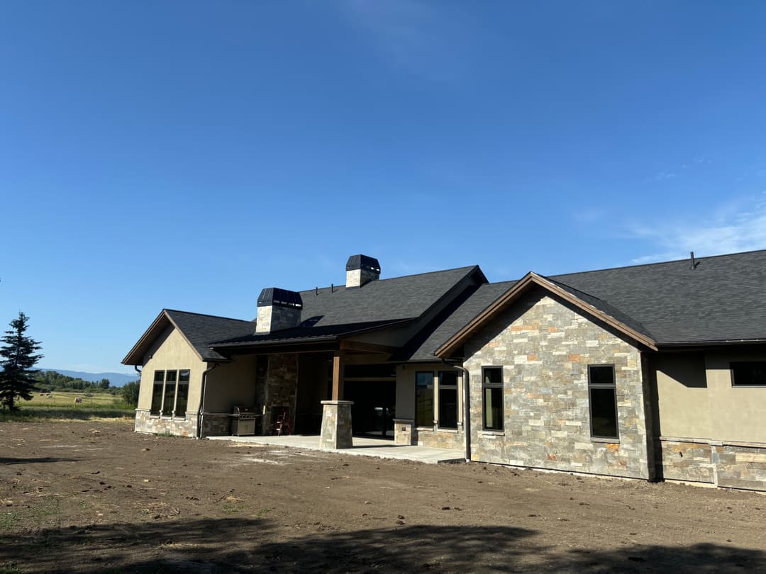 Modern rustic home with stone accents and large windows under a clear blue sky.