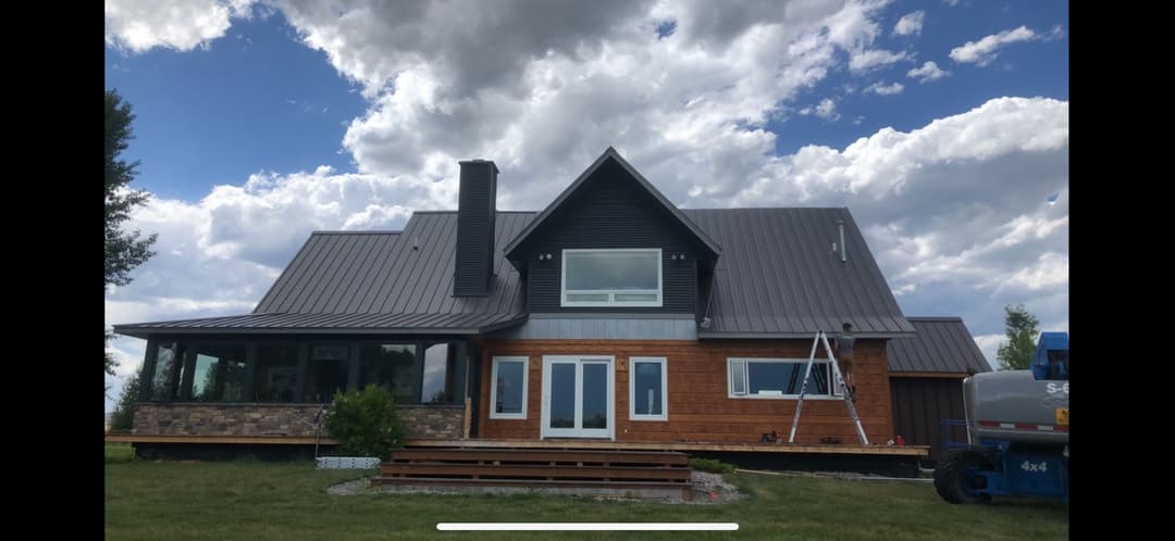 Modern mountain home with metal roof, large windows, and wooden accents under a cloudy sky.