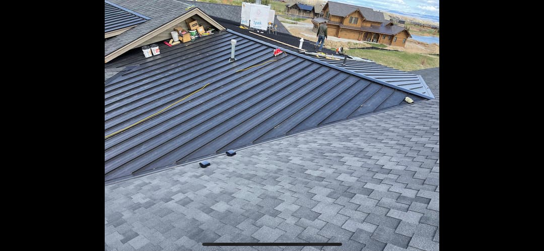 Roof installation in progress on a residential building with metal and shingled roofs.