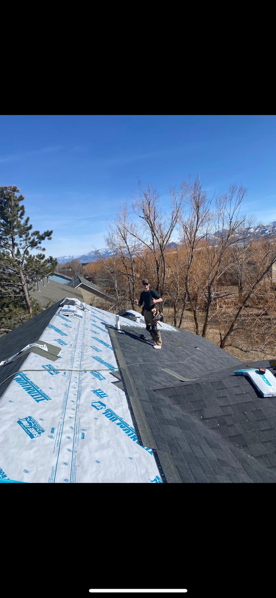 Roofing contractor working on a sloped roof installation under a clear blue sky.