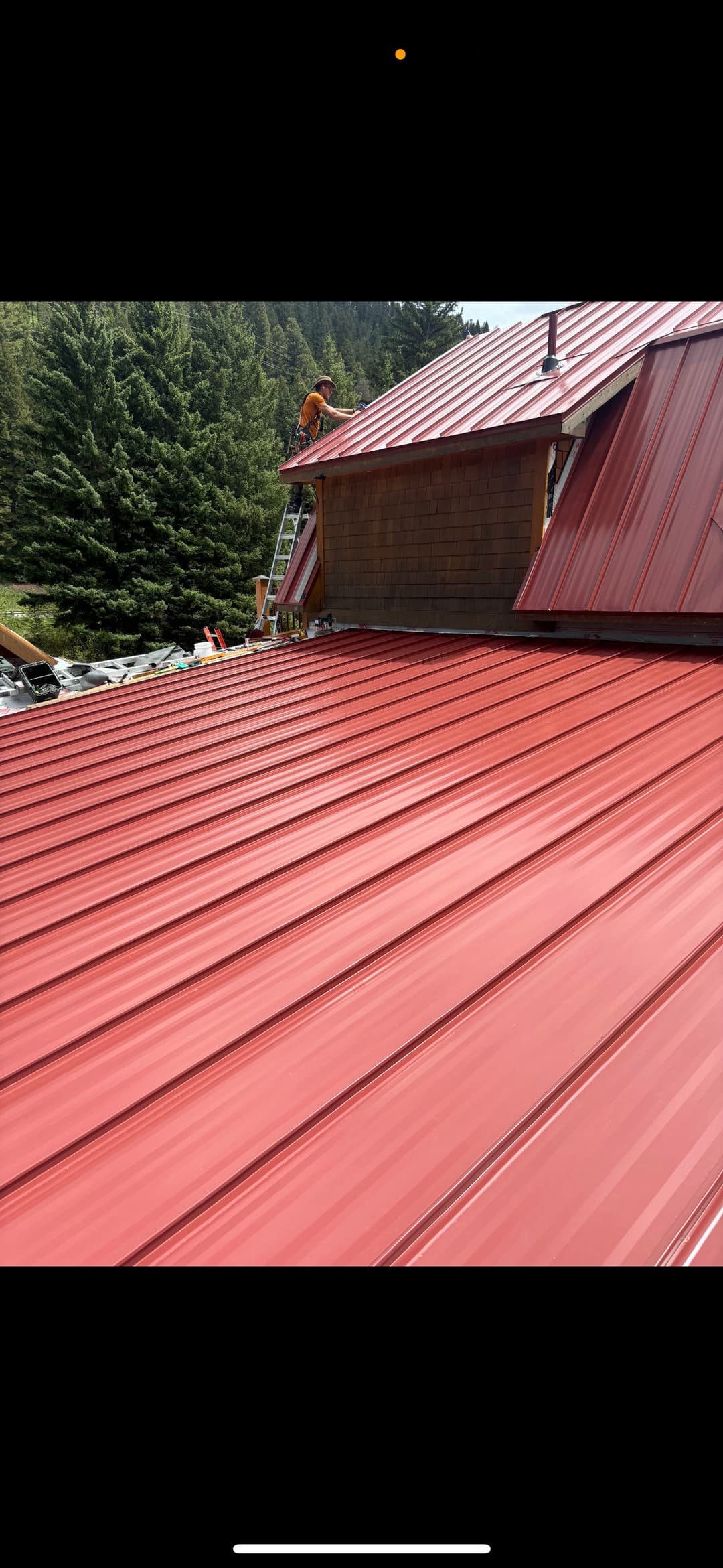 Red metal roofing installation on a house surrounded by evergreen trees.