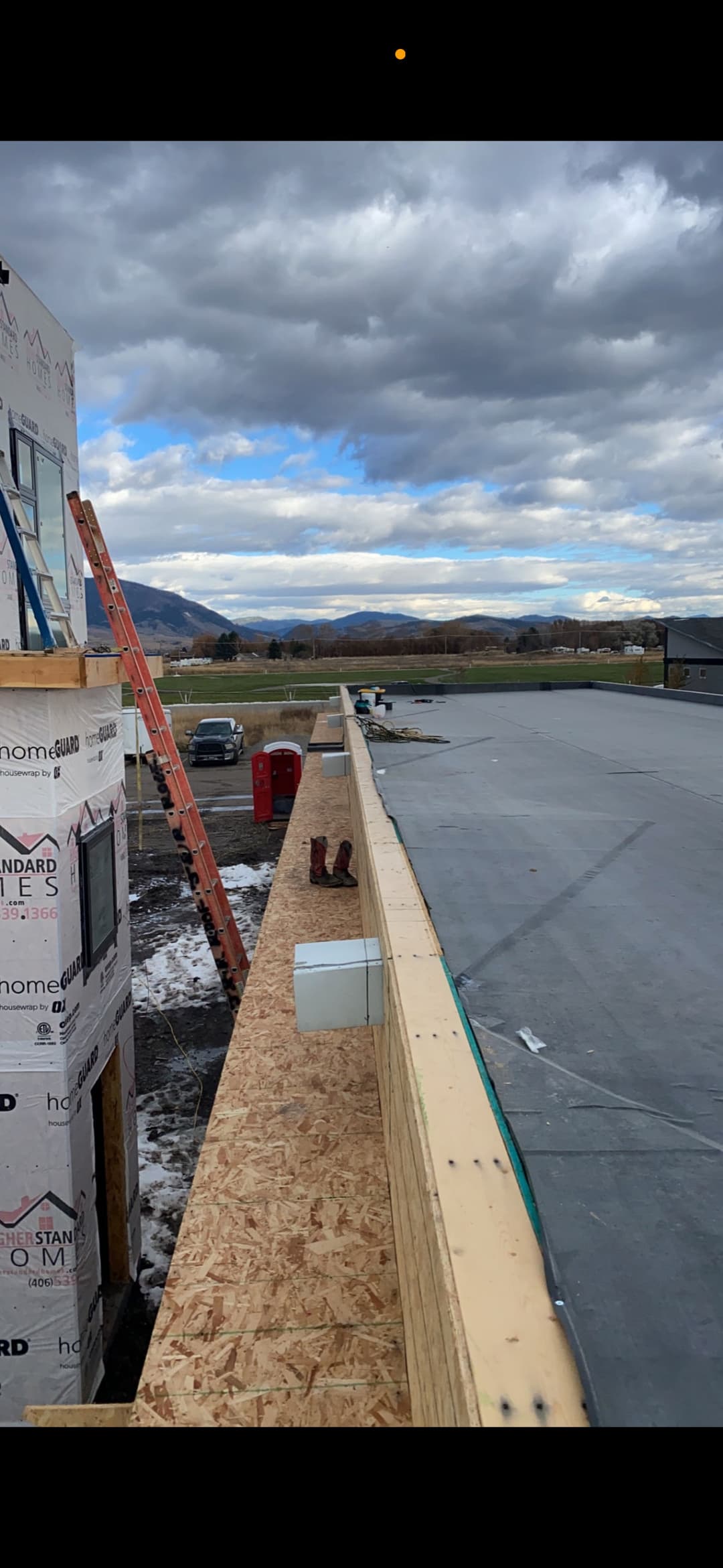 Construction site with a rooftop view, ladder, and mountains under a cloudy sky.