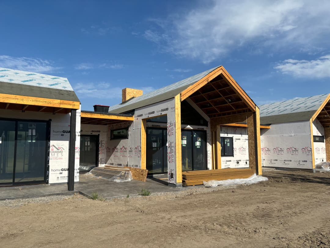 Modern house under construction with wooden accents and large glass windows against blue sky.